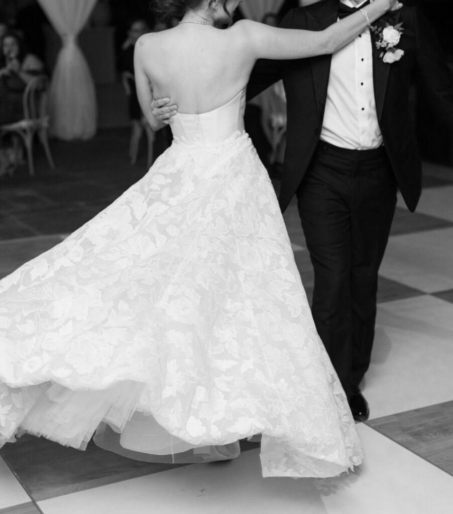 Bride twirls in gown on checkered dance floor.