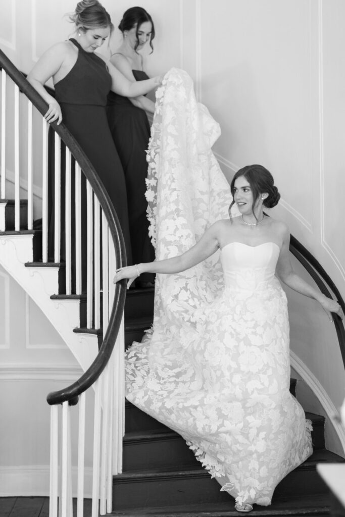 Bride descends stairs as bridesmaids carry her train.
