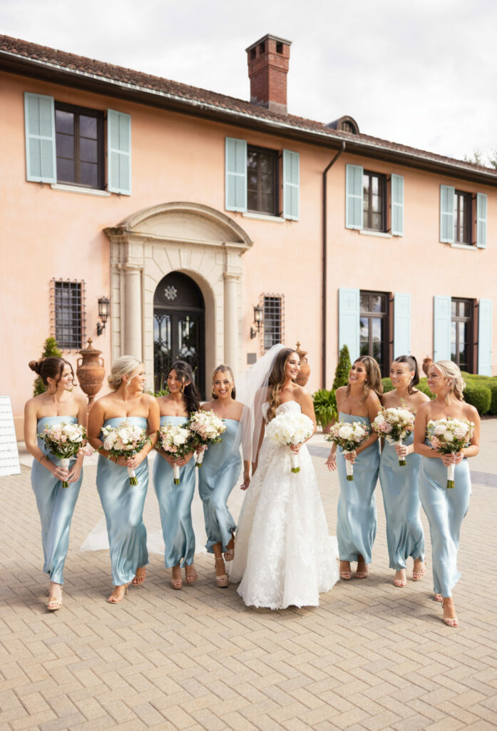 Bride and eight bridesmaids in blue by peach building.