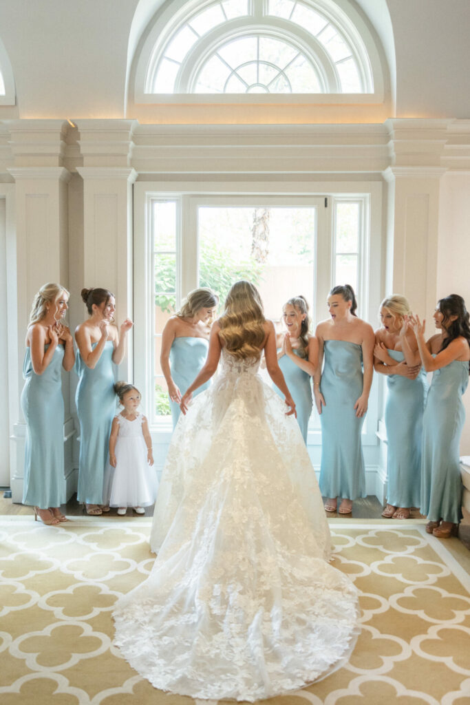 Bride in lace gown admired by bridesmaids and flower girl.