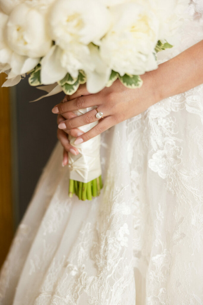 Katya Ruiz holds white bouquet in lace gown, ring visible.