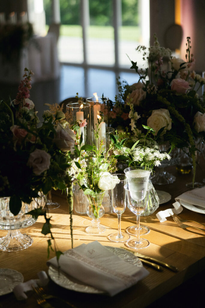 Elegant sunlit table with roses, candles, garden view.