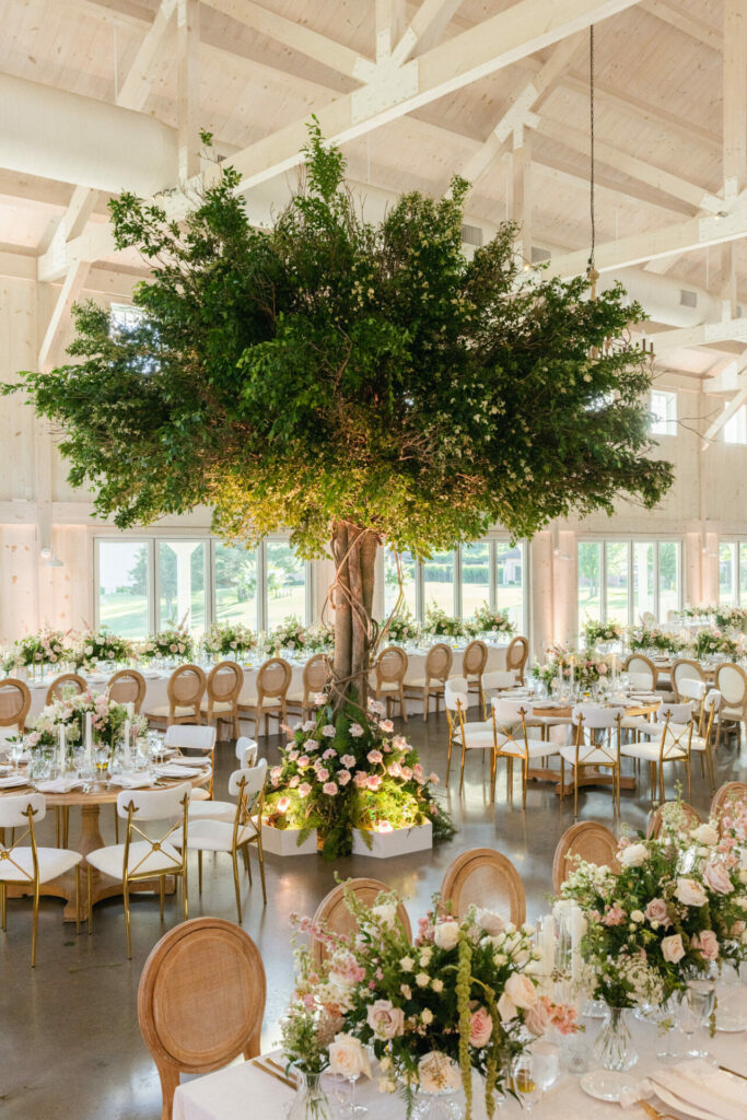 Chic event space with blush florals, gold chairs, tree centerpiece.