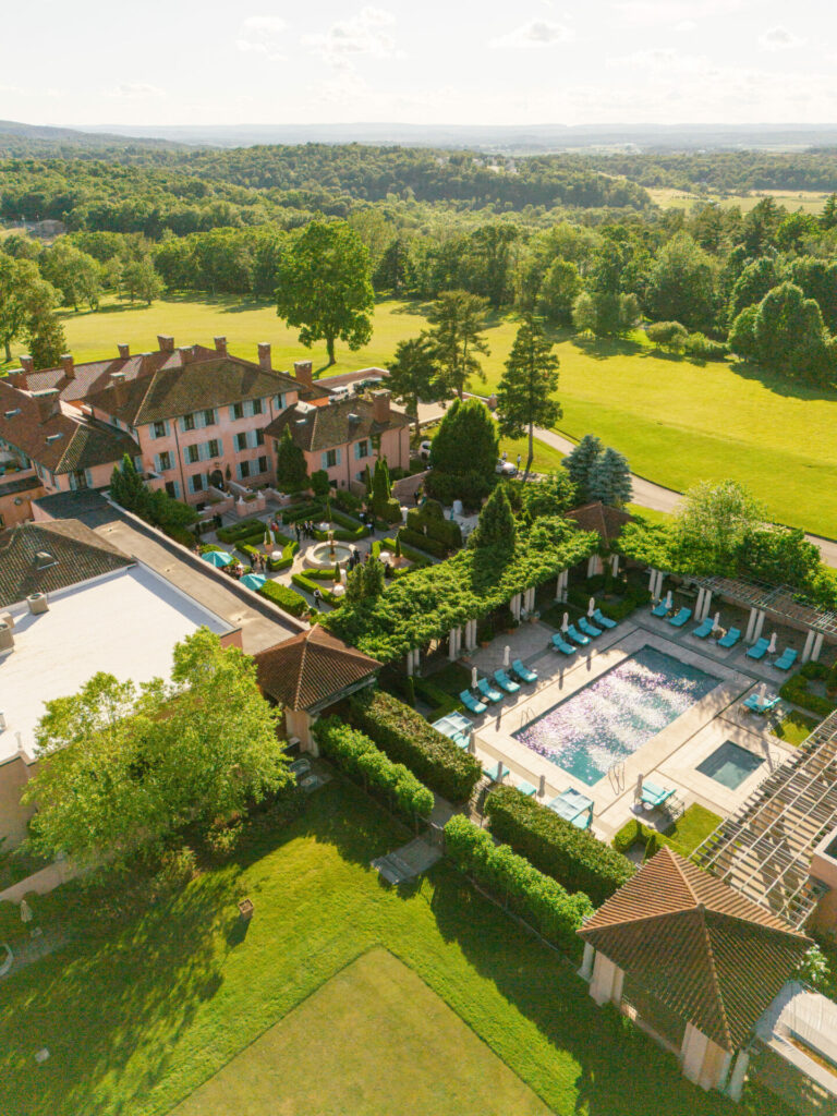 Aerial view, pink estate, gardens, and pool under clouds.