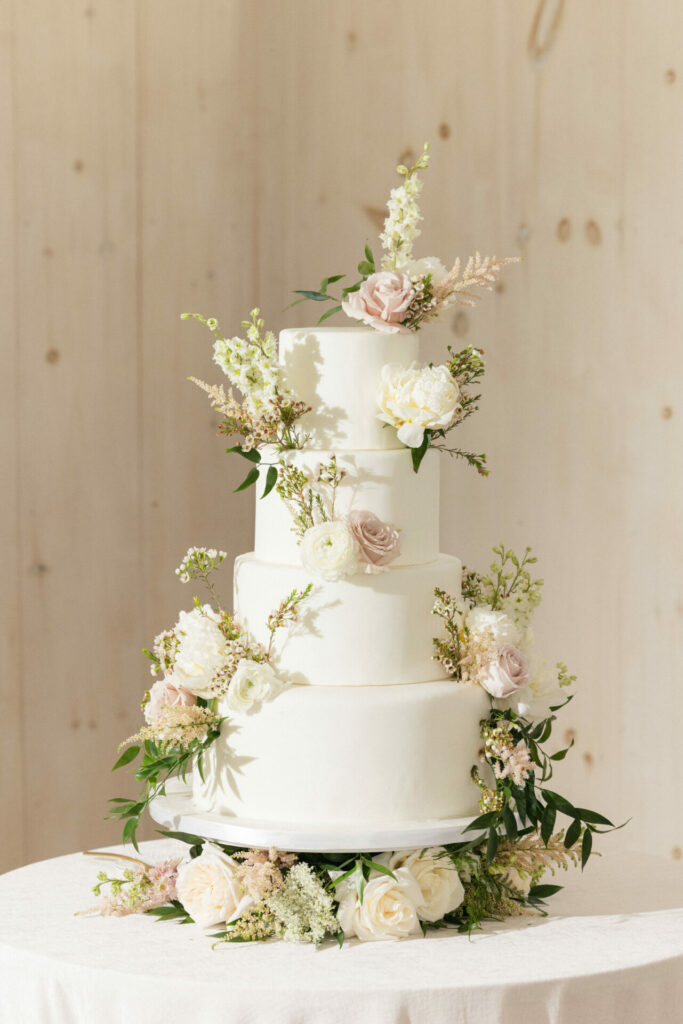 Elegant four-tier cake with pink, white flowers, greenery.
