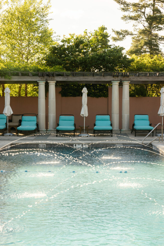 Luxury pool, turquoise chairs, pergola, lush greenery.