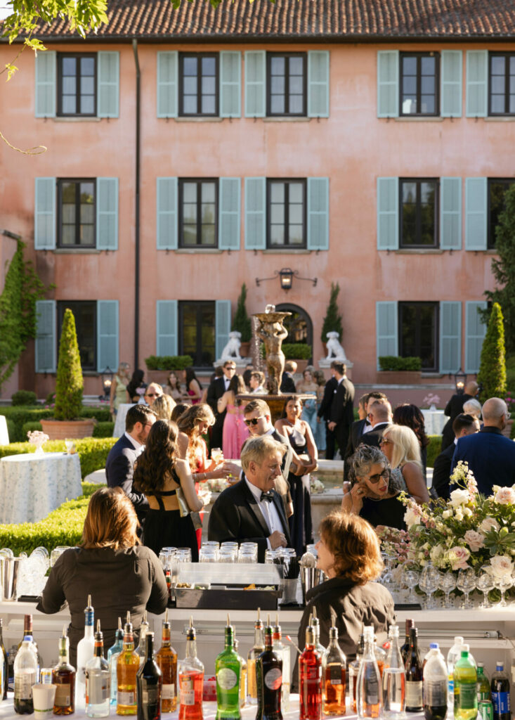 Garden event by pink villa, Katya Ruiz in bridal couture, guests mingling, bartenders serving drinks.