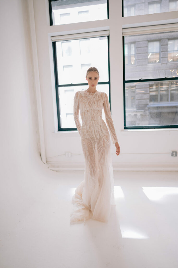 Bride in the sheer Anouka wedding dress by Mira Zwillinger in a bright room