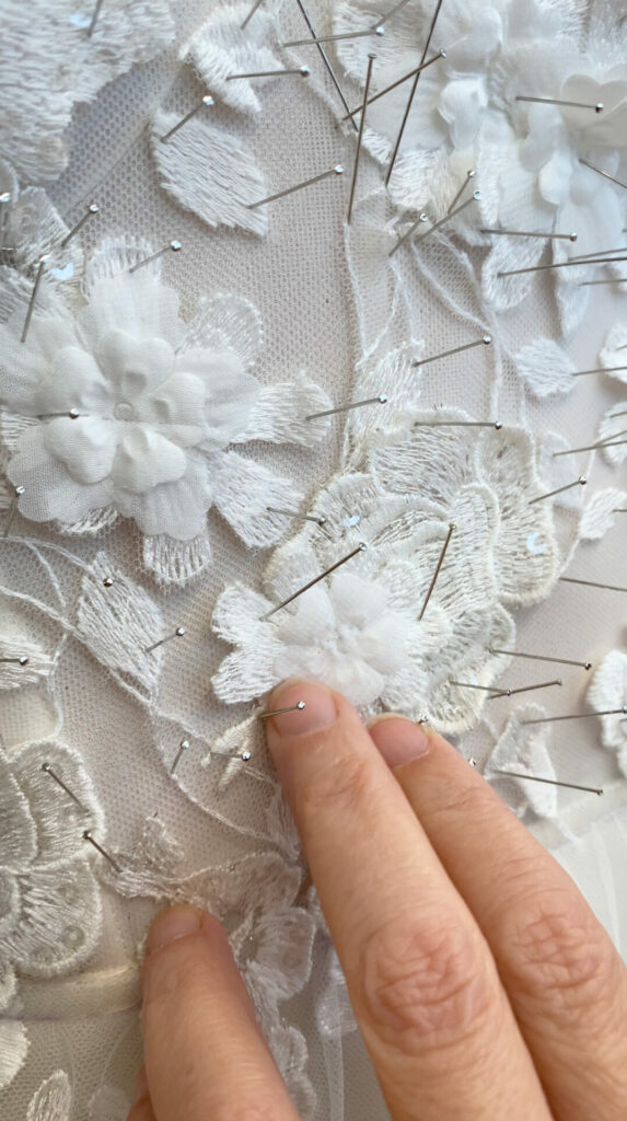 Hand touches embroidered white flowers on sheer mesh.