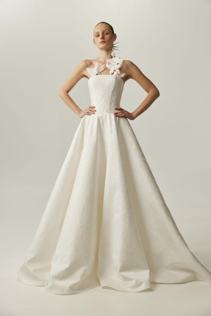 Woman in strapless white wedding dress, floral shoulder.