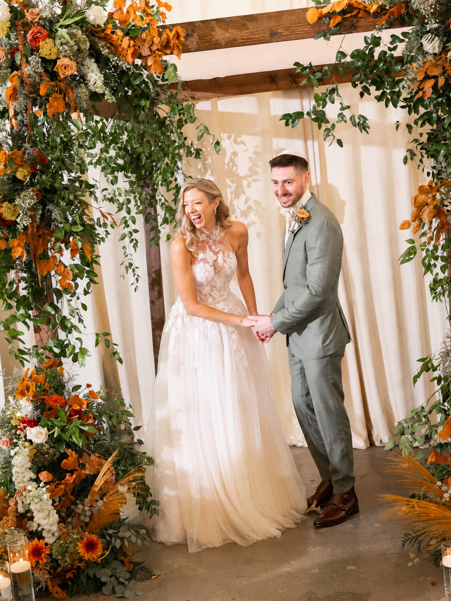 Bride and groom smiling under lush floral arch.