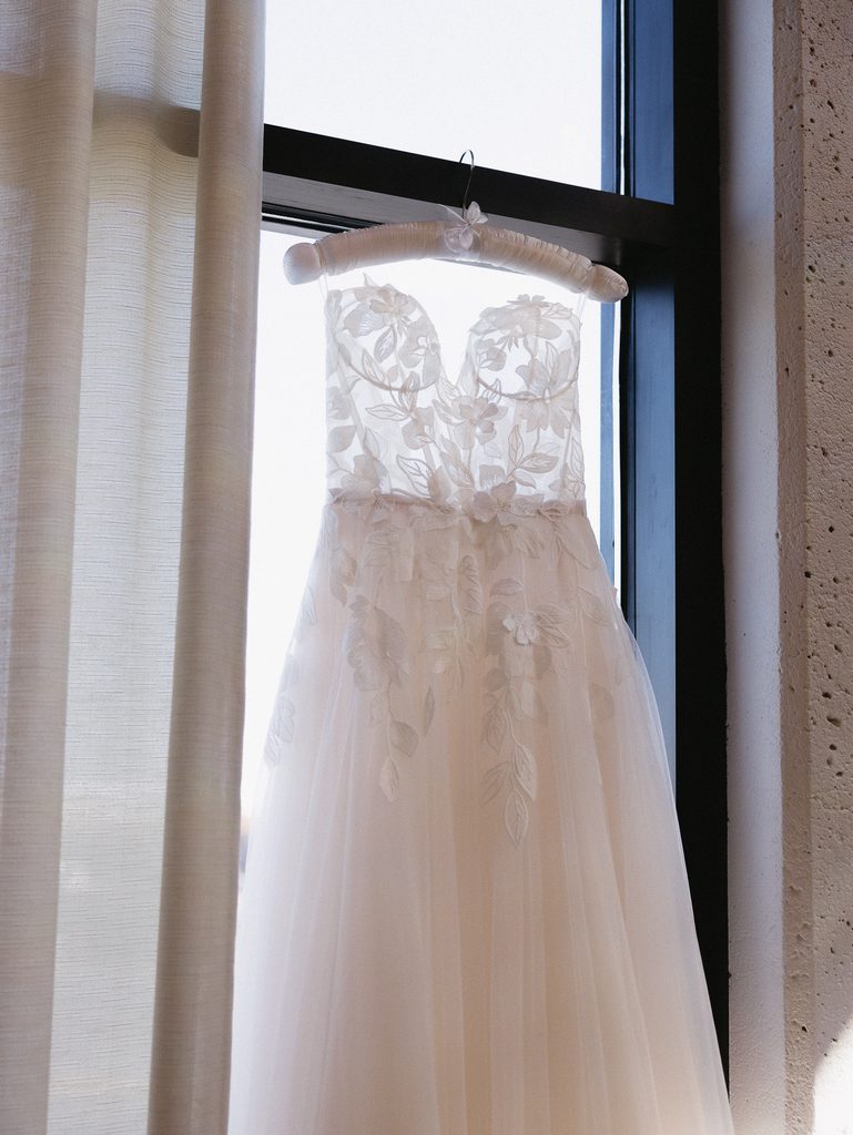 White lace wedding dress on hanger, sunlight shining.