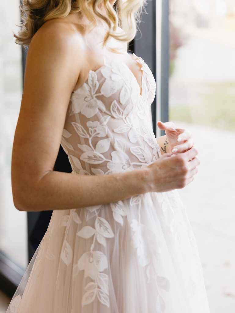 Bride in floral lace dress by a window.