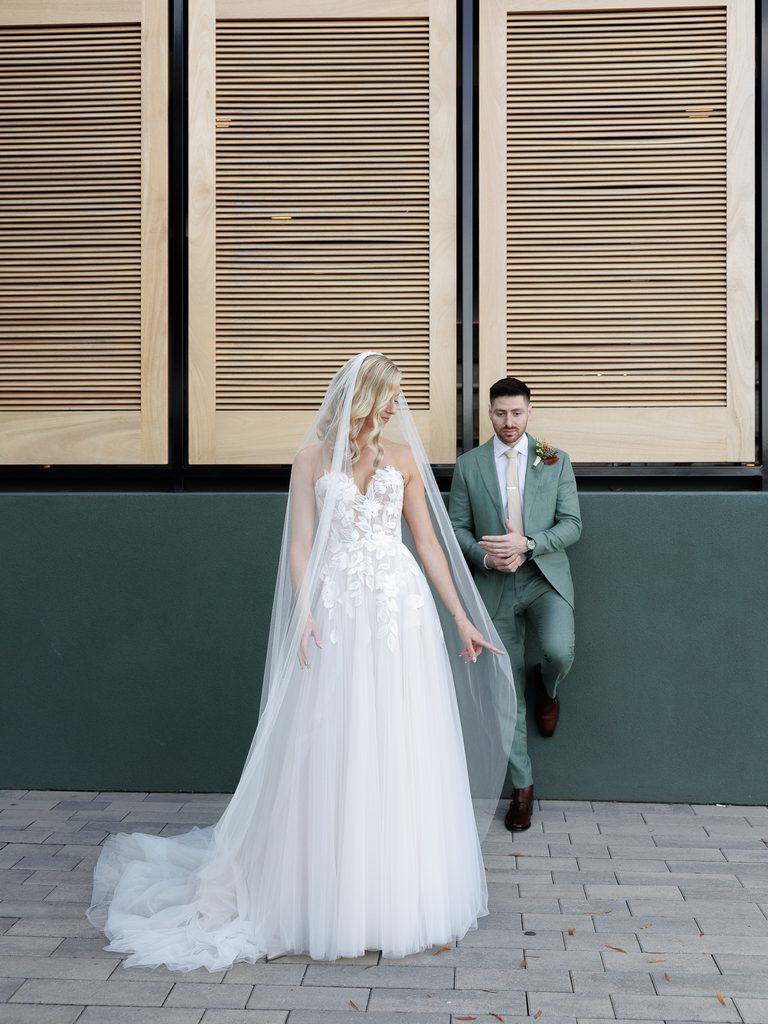 Bride in white, groom in green, modern backdrop.