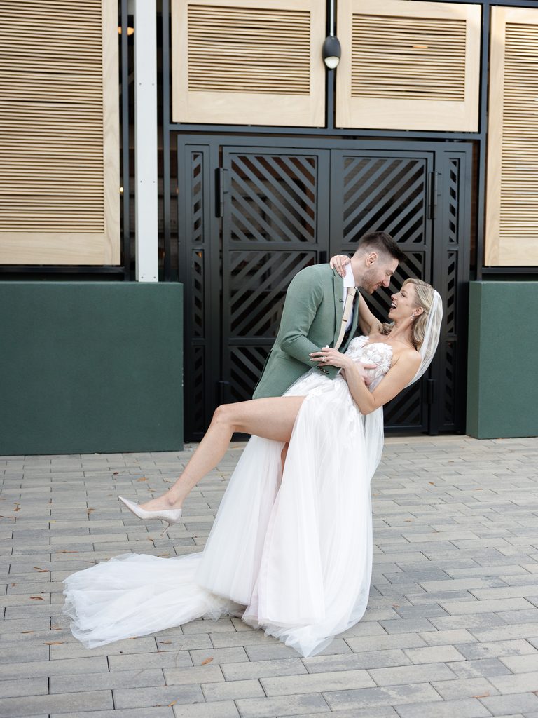Groom dips bride in couture dress outdoors.