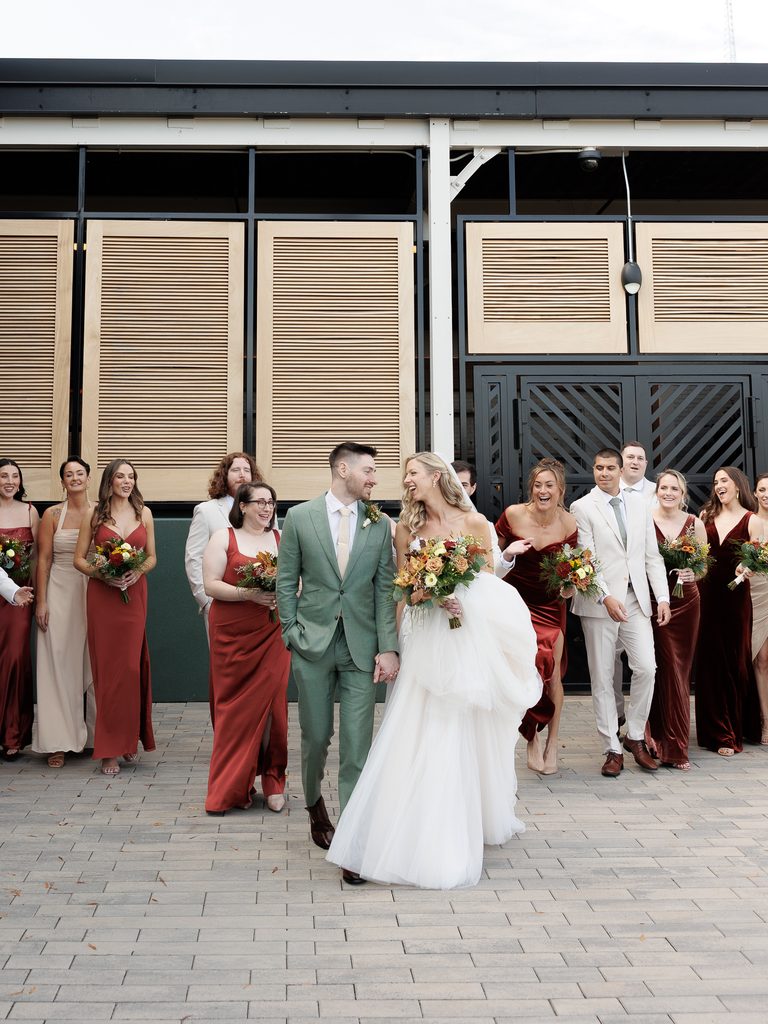 Elegant wedding party smiles outside modern building.