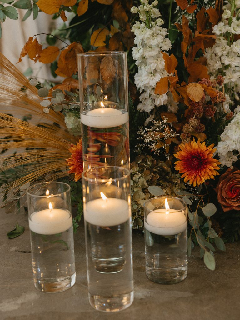 Lit floating candles in glass vases, autumn florals.