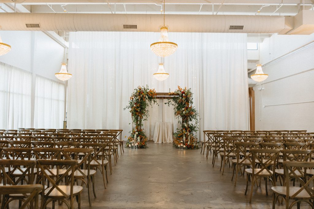 Chairs face floral arch in elegant wedding room.