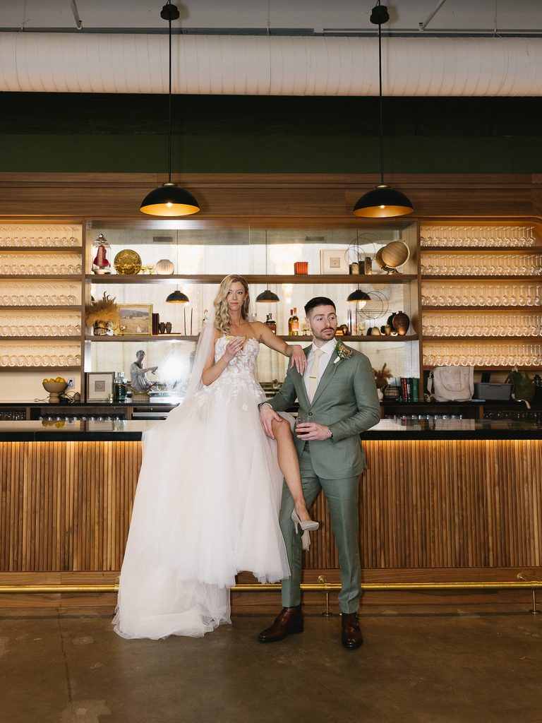 Bride poses on groom by modern bar.