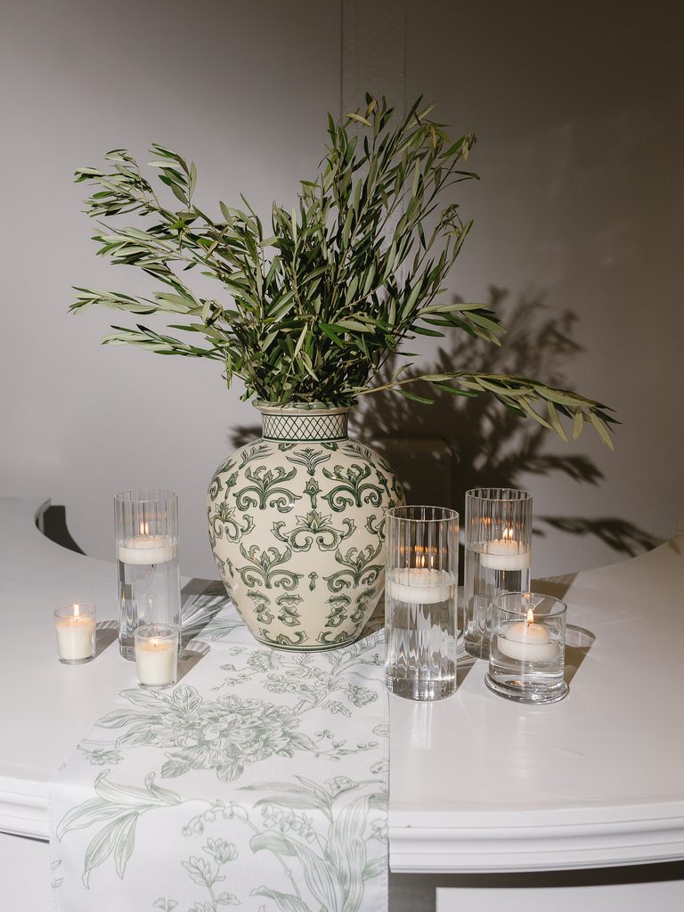 Elegant vase with candles on white floral table.