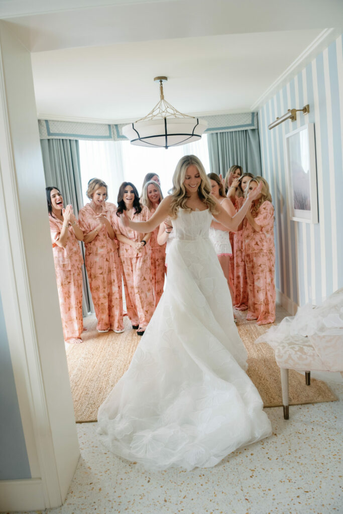 Bride twirls, bridesmaids cheer in bright room.