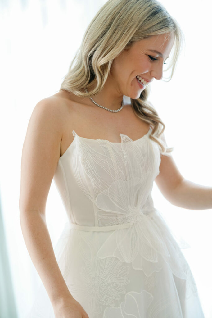 Elegant blonde bride in floral strapless dress smiles.