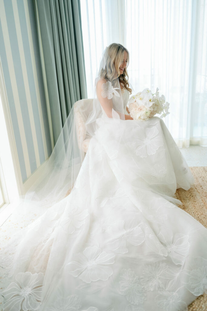 Bride in floral gown with bouquet, soft light silhouette.