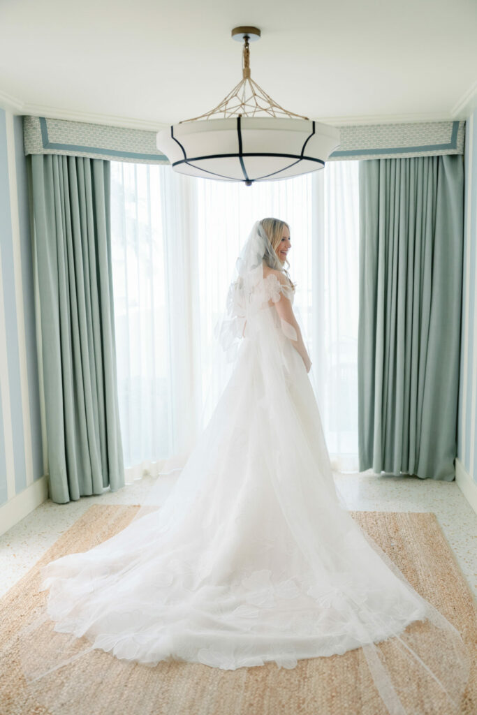Bride in luxury gown by sunlit windows.