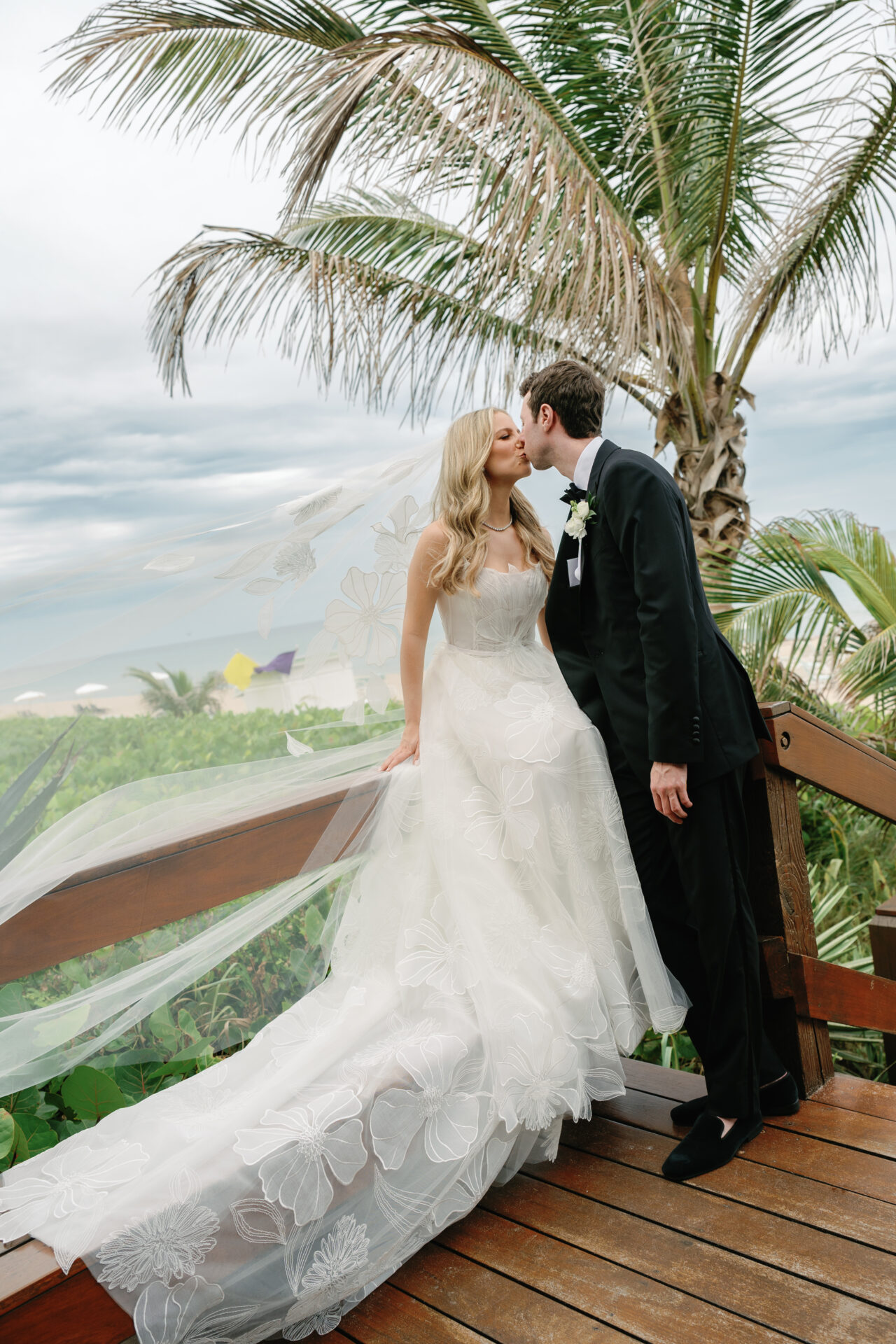 Bride and groom kiss on beachside wooden steps.
