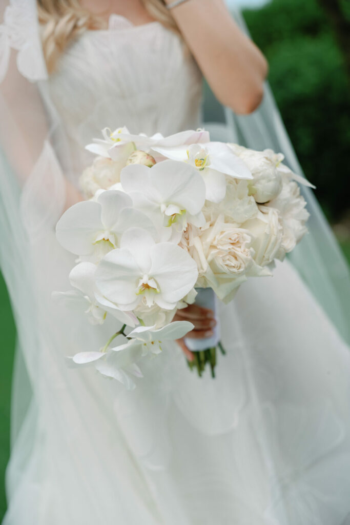 Bride in white with orchid-rose bouquet outdoors.