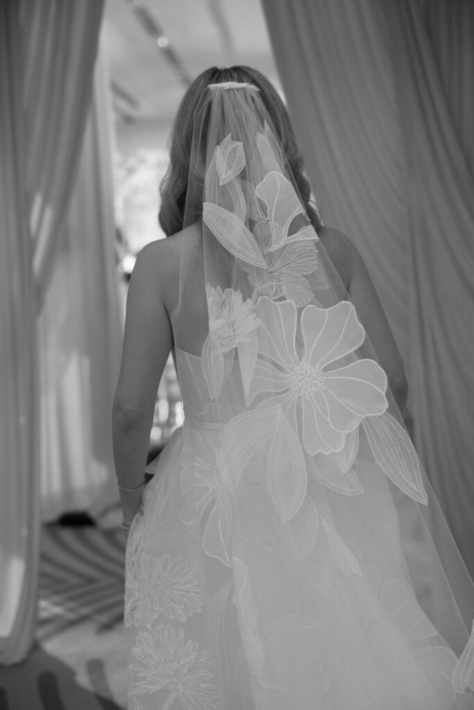 Bride in floral veil, back turned, softly lit.