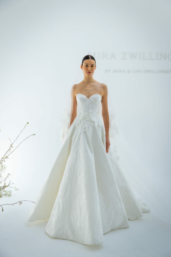 Woman in white strapless dress, green branches nearby.
