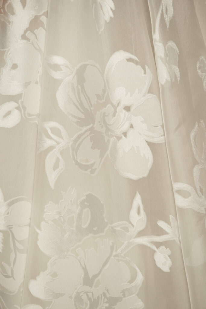 Sheer beige fabric with raised white floral pattern.
