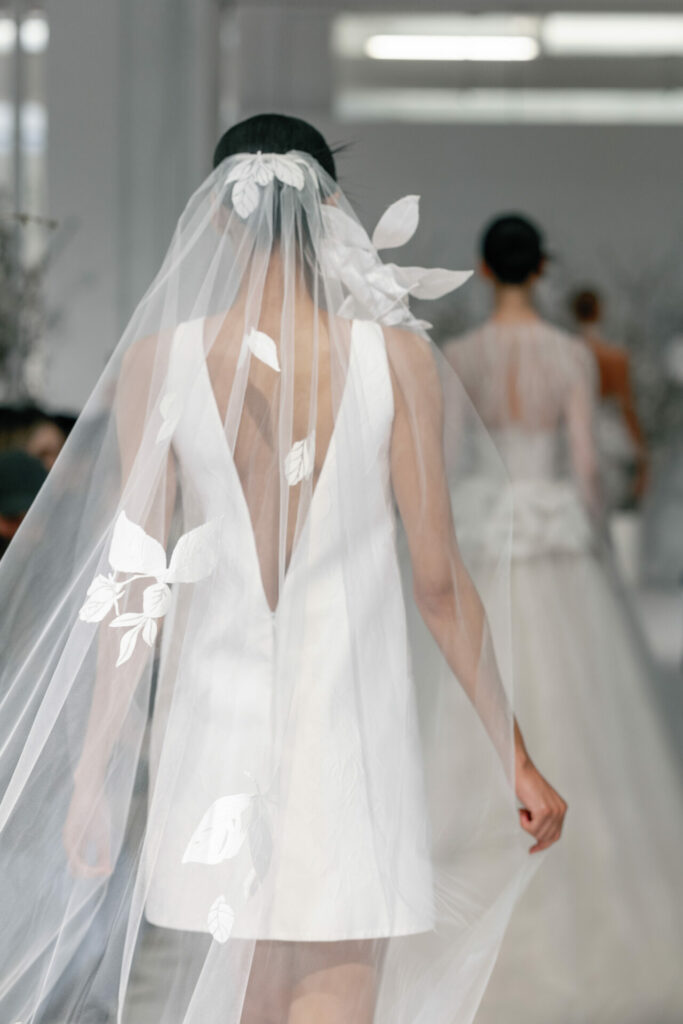 Model in short white Clea dress and veil on runway.