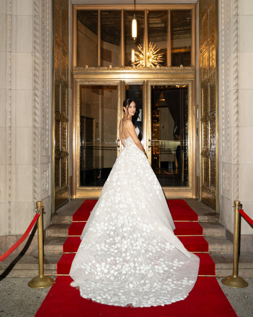 Woman in white floral gown on red carpet.