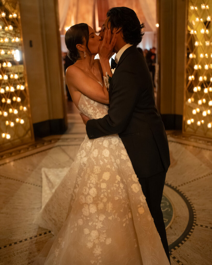 Bride and groom kiss under golden, dreamy lights.