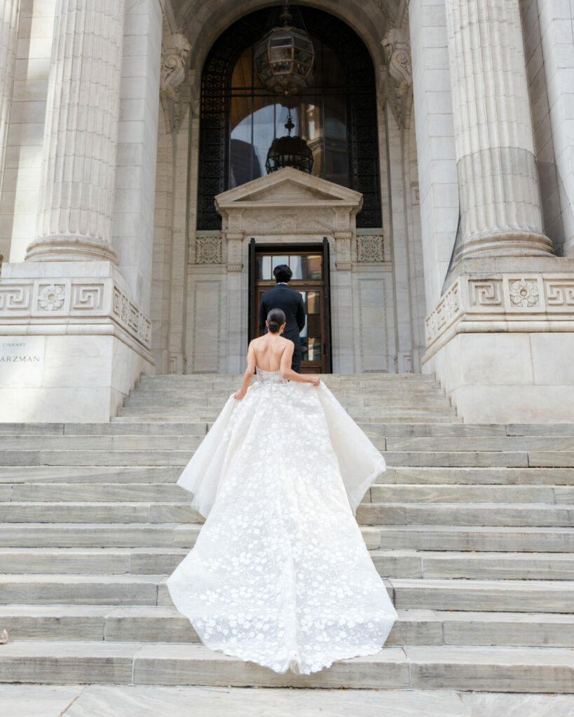 Bride in couture gown climbs grand ornate steps.