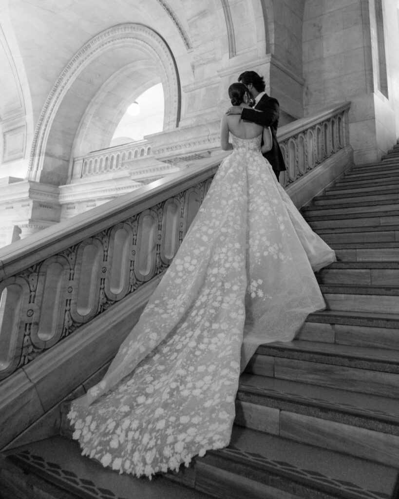 Couple embraces on marble stairs; bride in couture gown.
