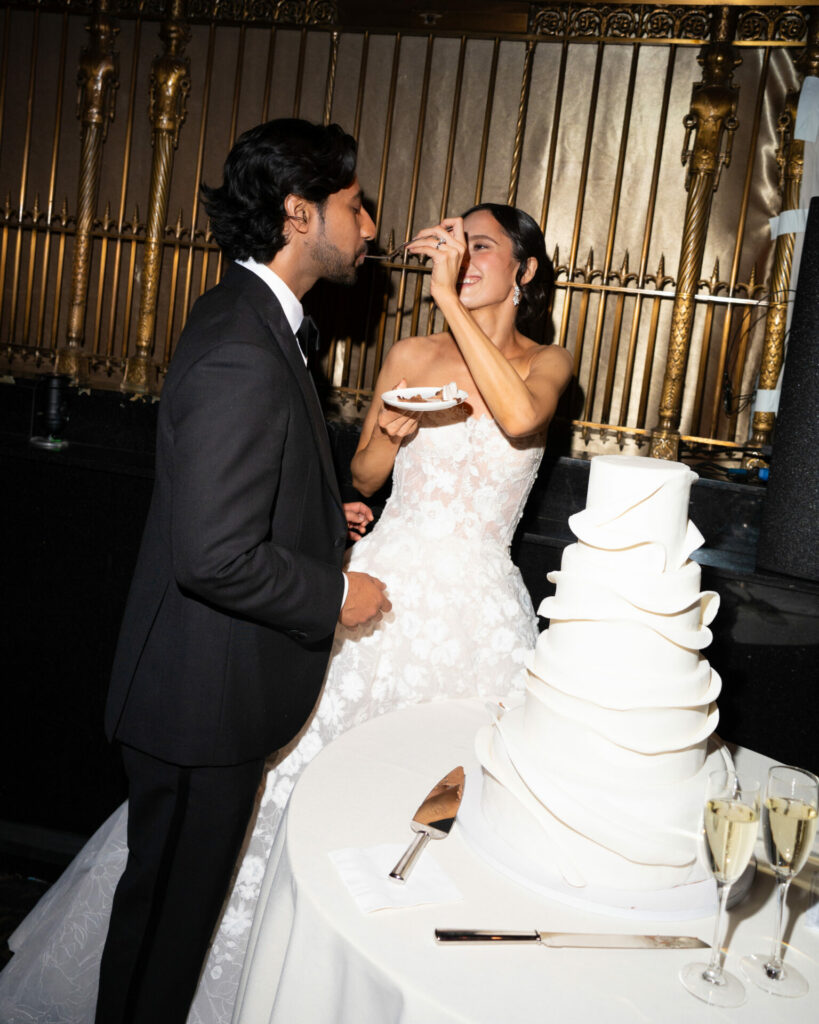 Bride feeds groom cake by elegant wedding table.