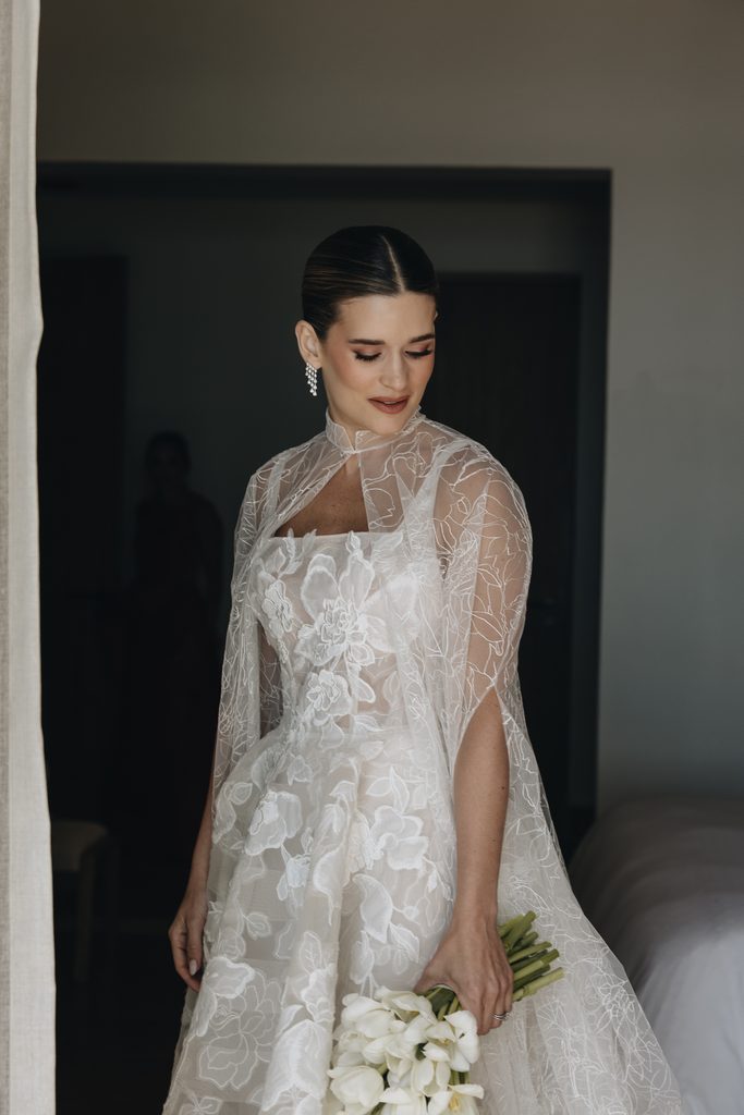 Bride in lace dress and cape, smiling down.