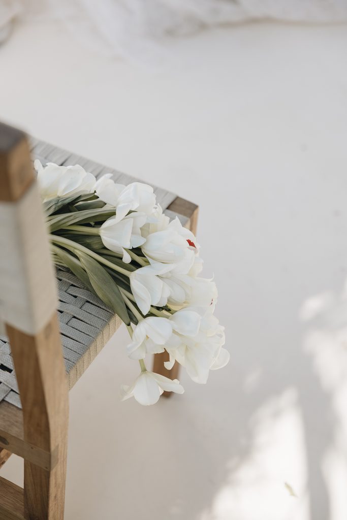 White tulip bouquet on woven chair, minimal background.