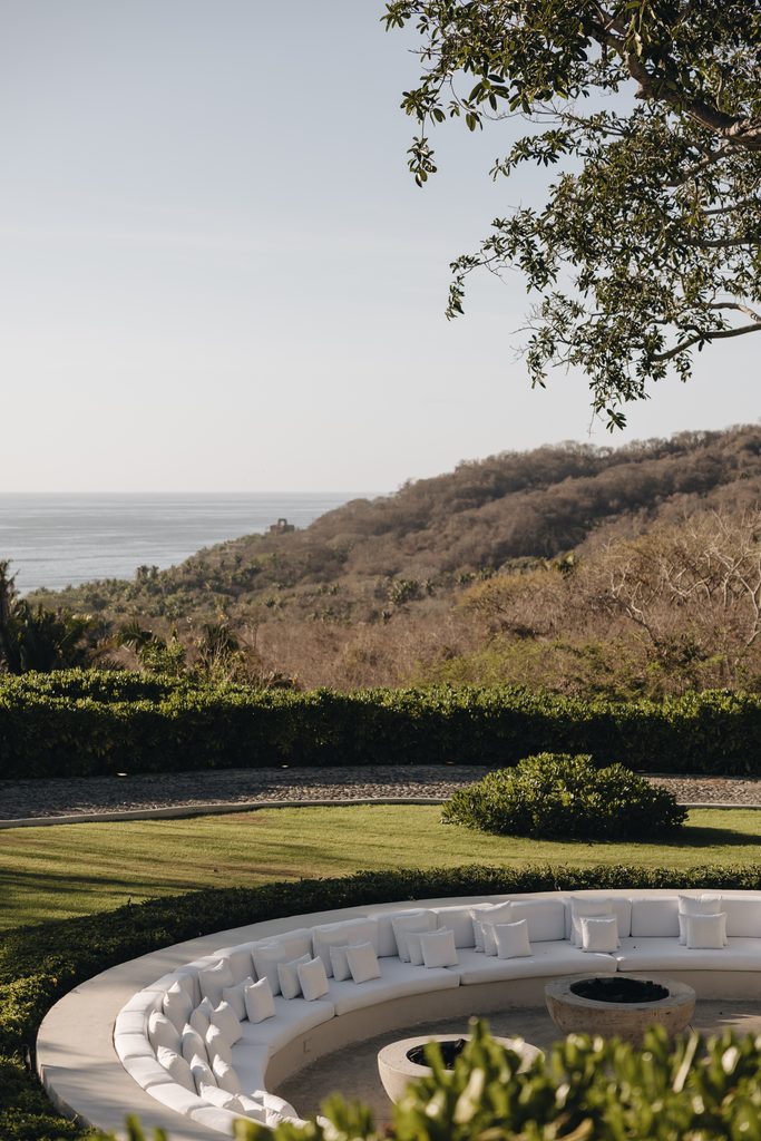Curved seating, white cushions, fire pit, ocean view.
