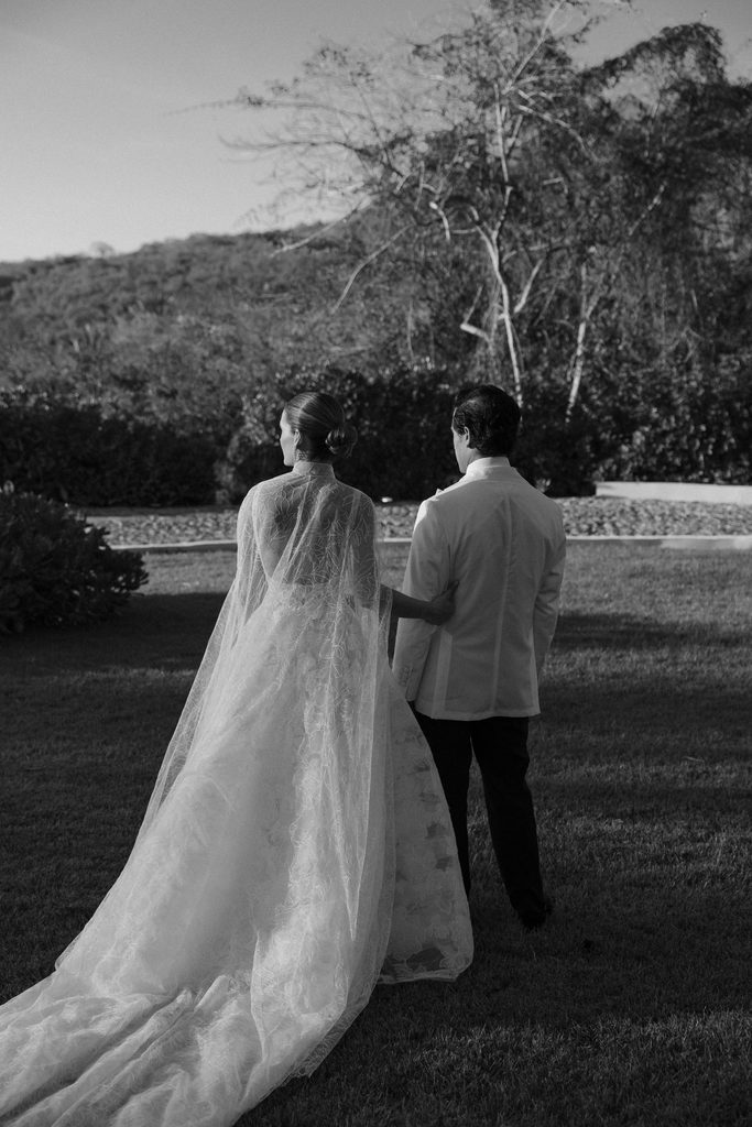 Bride and groom on grass, elegant outdoor setting.