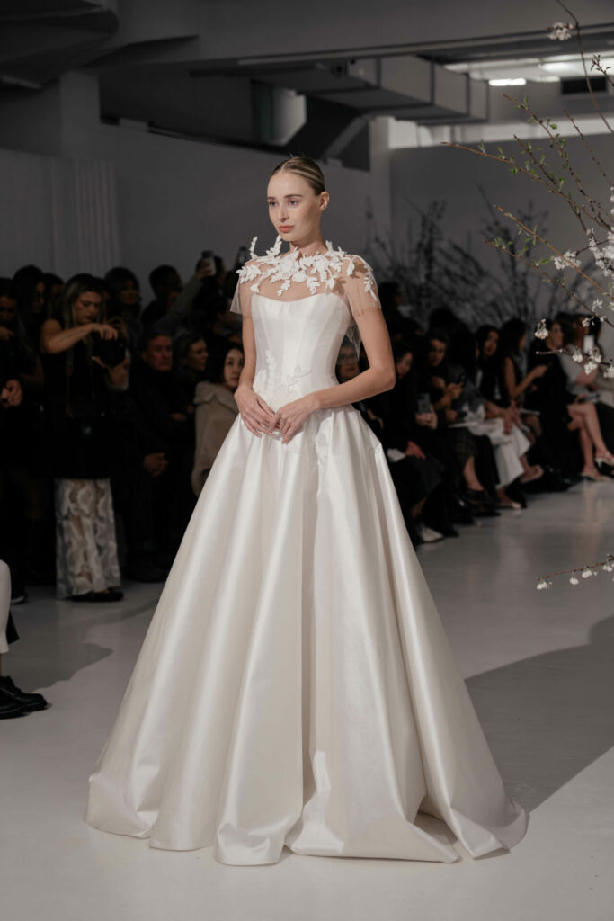 Model in white satin gown walks runway.