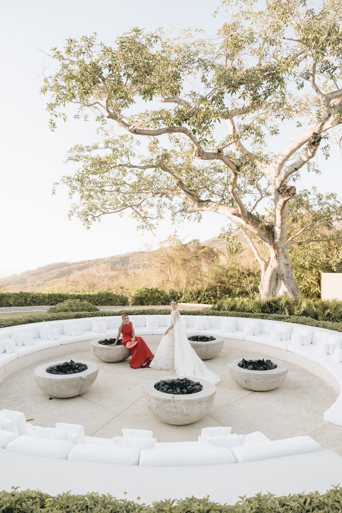 Bride and guest seated by fire pits outdoors.