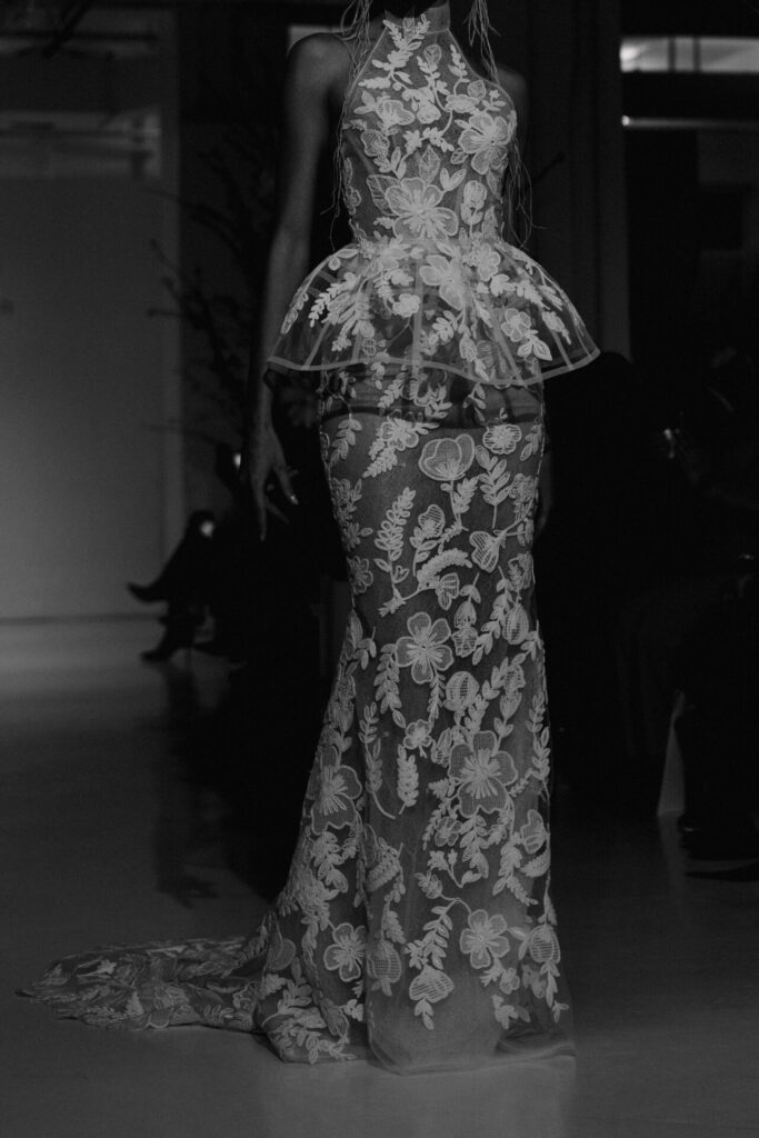 Model in sheer embroidered dress on black-and-white runway.
