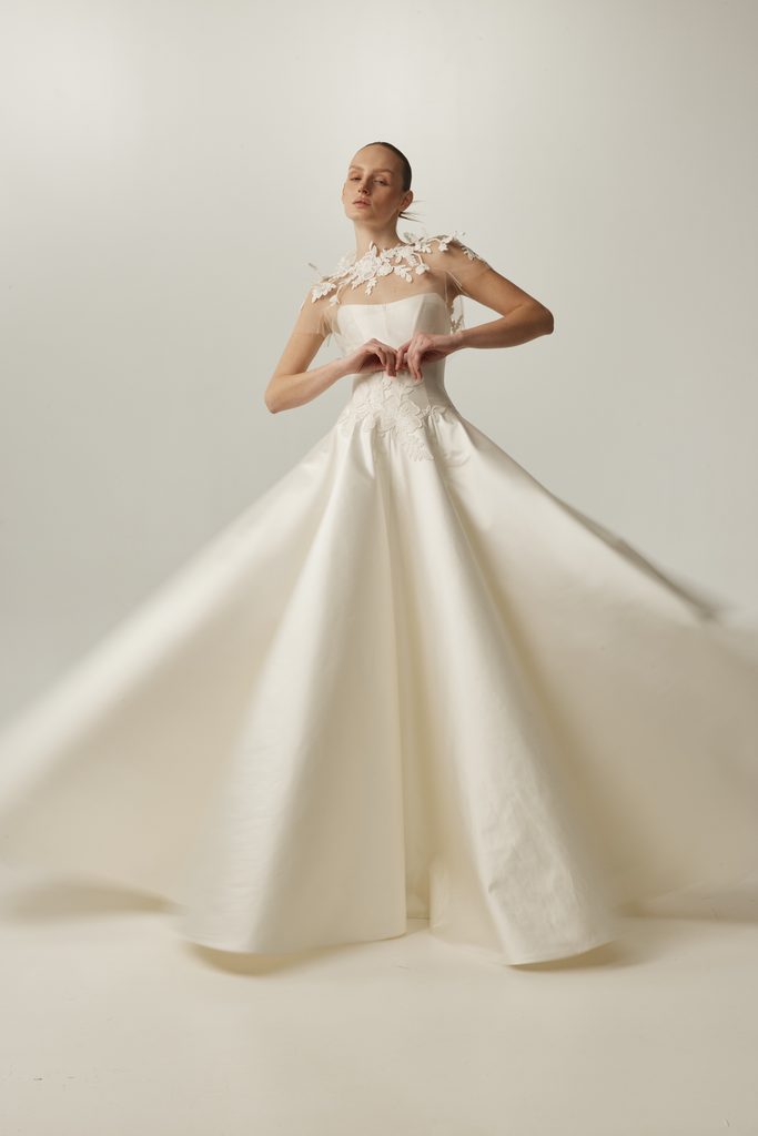 Woman in floral white gown forms heart at waist.