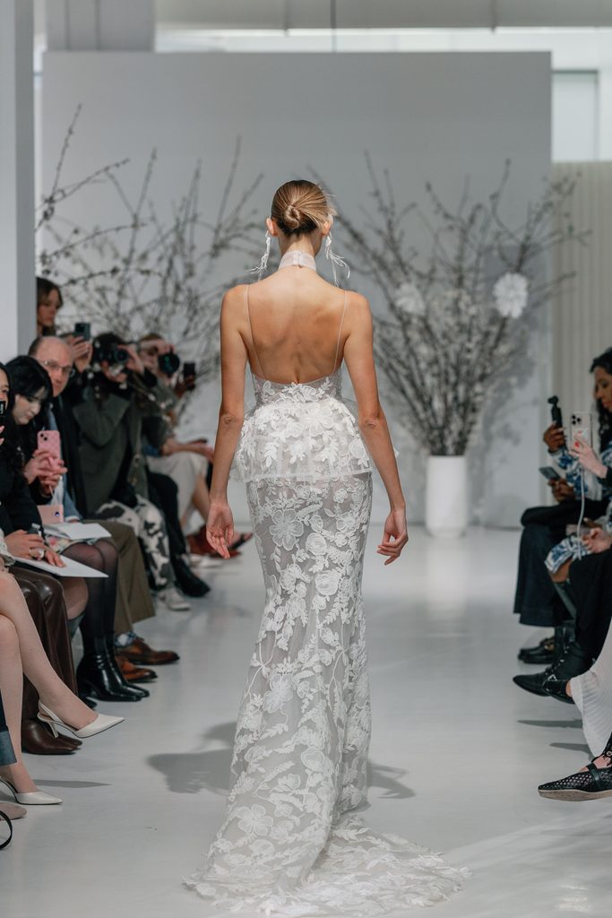 Model in lace gown on runway, audience watching.