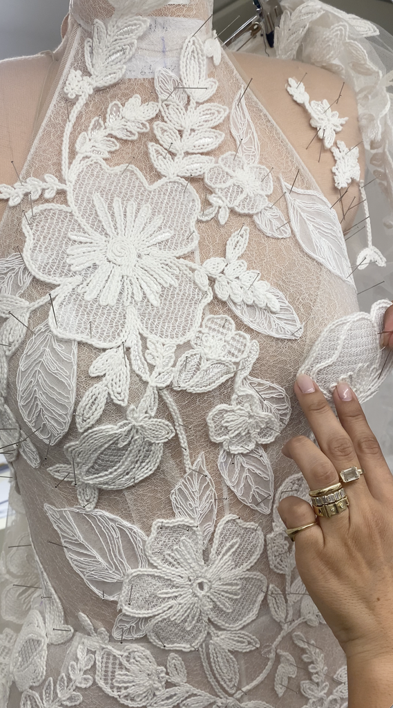 Hand with rings pins floral lace to mannequin.
